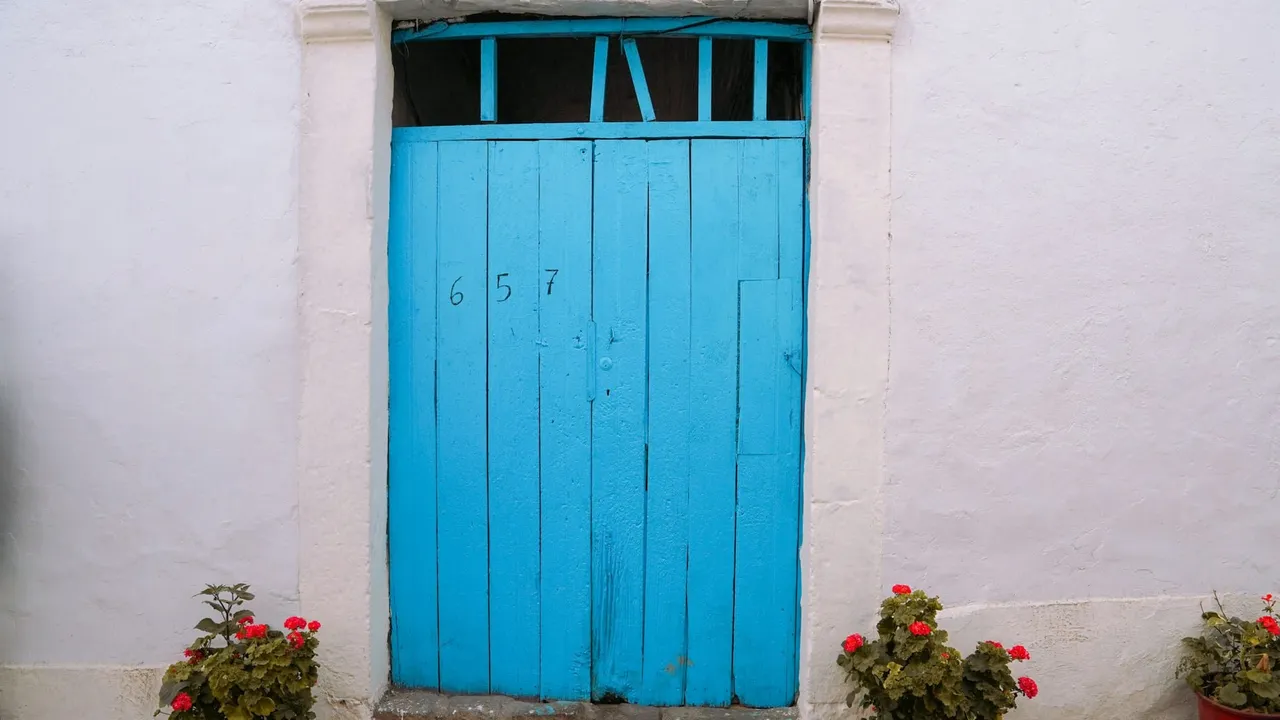 Puerta de madera azul de una casa encalada con geranios rojos