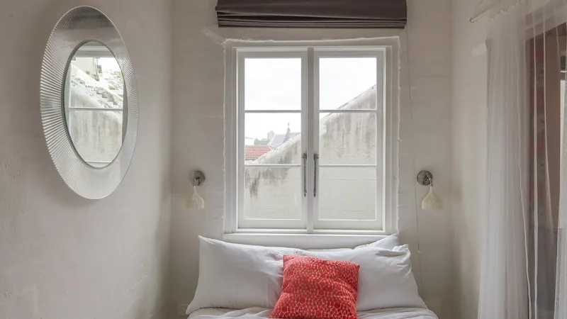 Dormitorio pequeño con paredes pintadas de blanco, una ventana, una cama y un aplique a cada lado