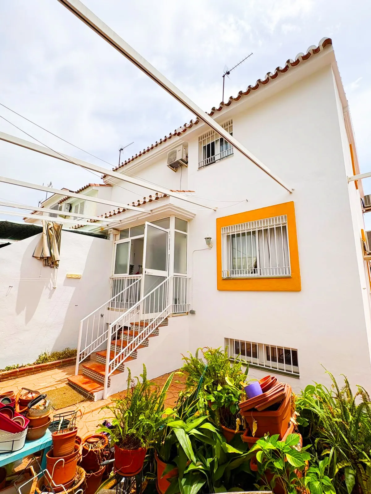 Fachada trasera y patio de una casa pintados en blanco, con el recercado de la ventana en mostaza